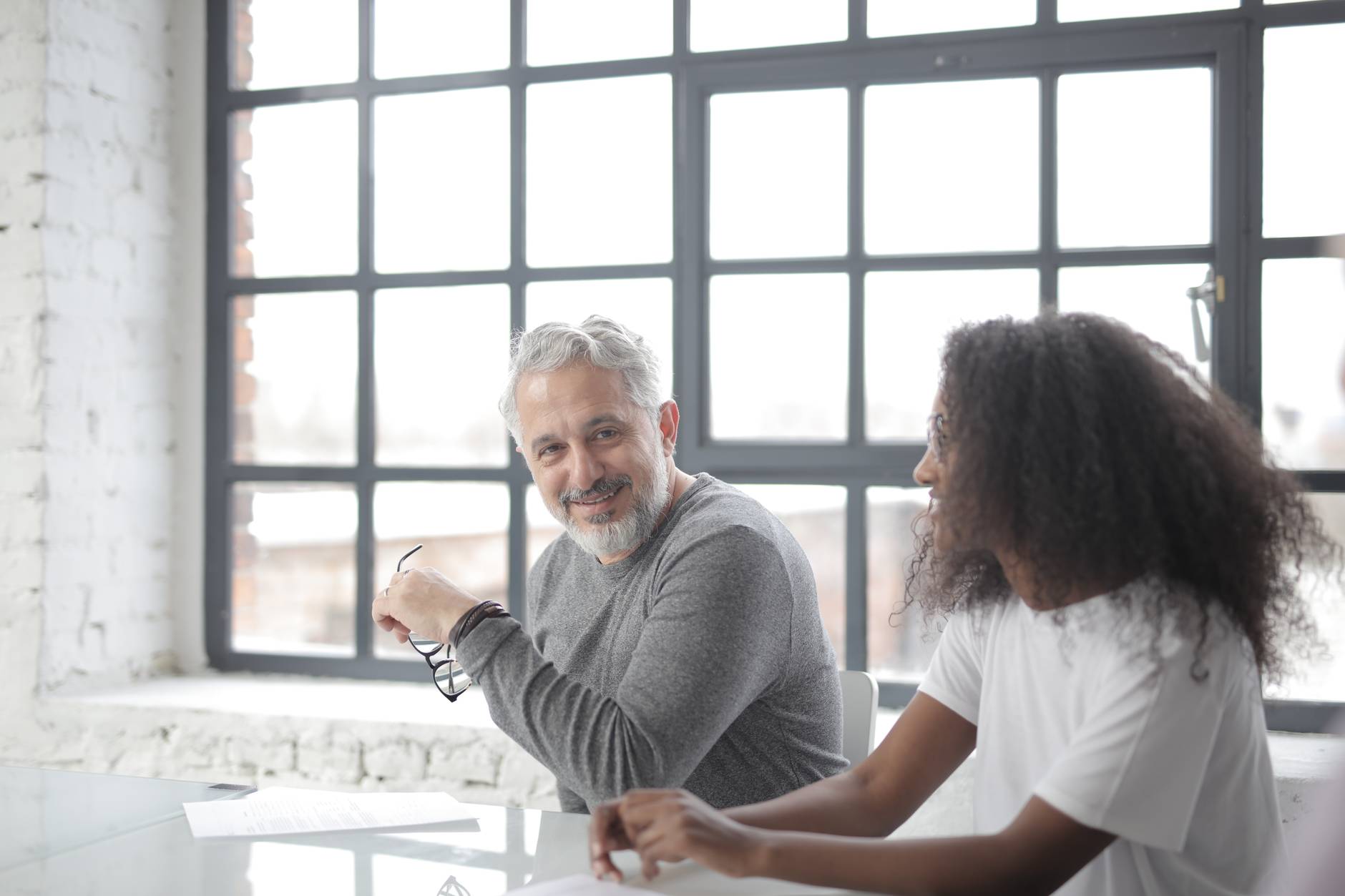 cheerful senior gray haired mentor supporting young black colleague in office