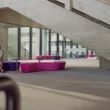 Frau sitzt entspannt auf einer violett-pinken Sitzbank in einem modernen, lichtdurchfluteten Gebäude mit Betonarchitektur und großer Treppe im Hintergrund.