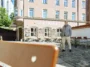 Businessporträt eines Mannes vor dem Restaurant Emmi’s Kitchen in Augsburg. Er steht auf einem historischen Platz mit Blick zur Seite, eingerahmt von Altstadtarchitektur und einer Kirche im Hintergrund.